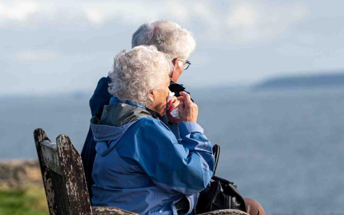 Two elderly people sitting on a bench looking at the sea